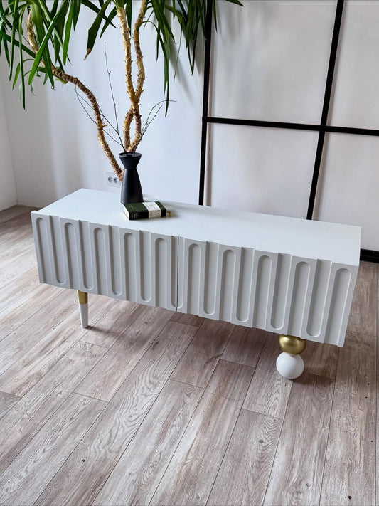 وحدة تلفاز أورا مودرن أبيض ثلجي بتصميم مشرّح (Fluted) وقاعدة كروية ذهبية من رحايا لغرفة المعيشة.