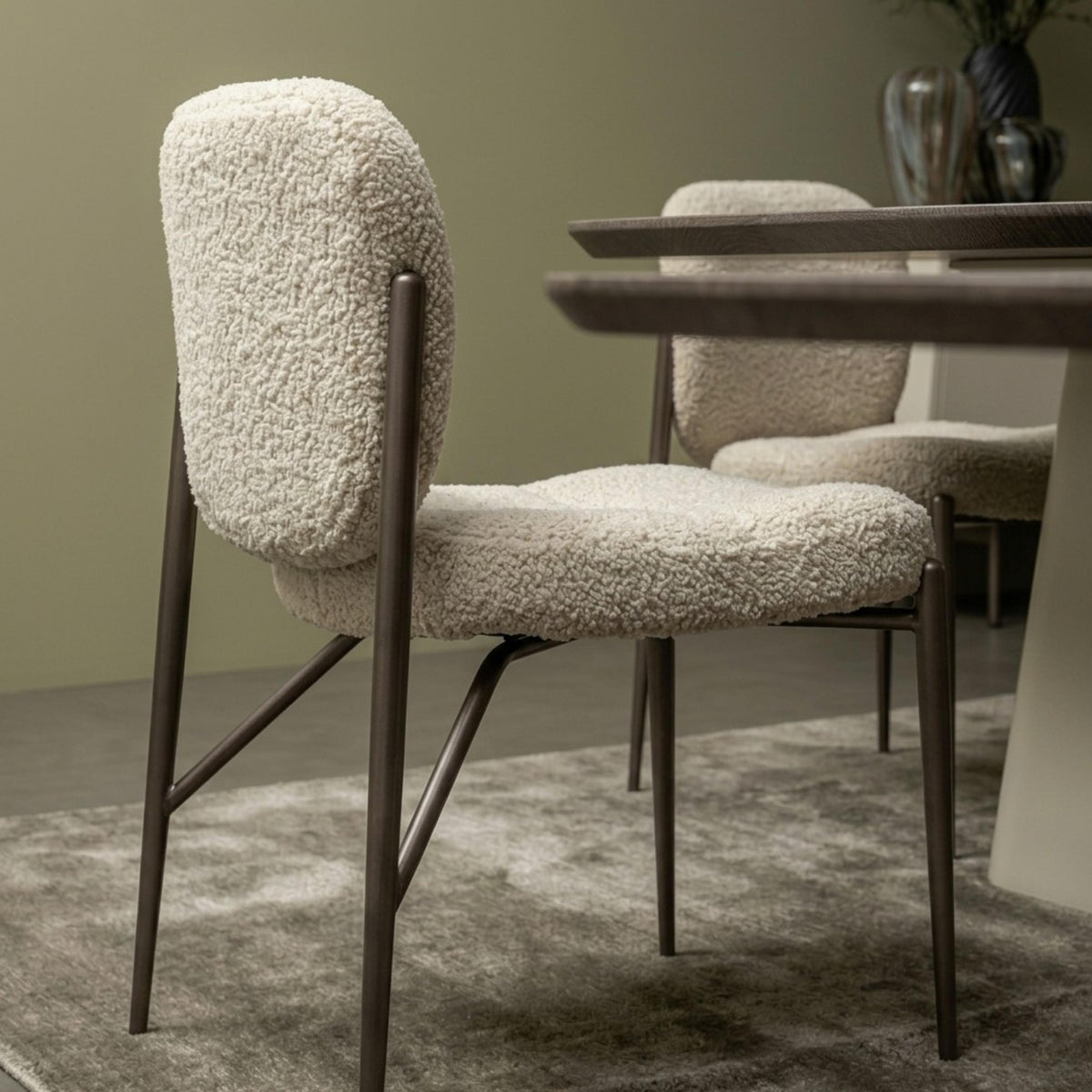 Modern dining chair with cream textured bouclé upholstery and a dark frame placed beside a wooden dining table.