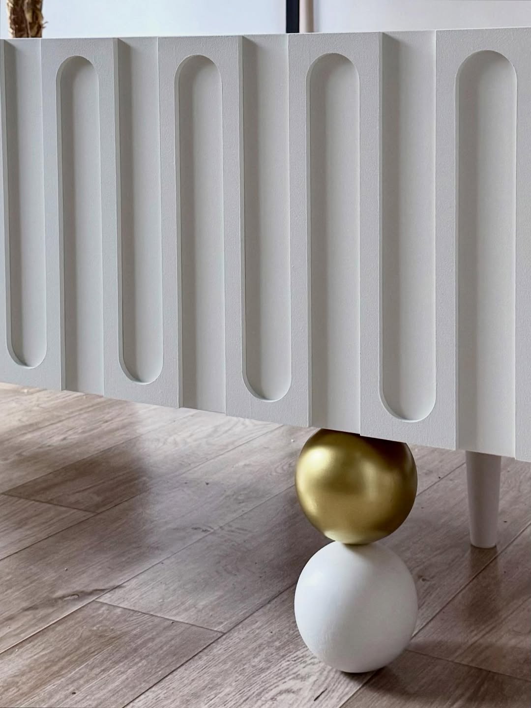 وحدة تلفاز أورا مودرن أبيض ثلجي بتصميم مشرّح (Fluted) وقاعدة كروية ذهبية من رحايا لغرفة المعيشة.